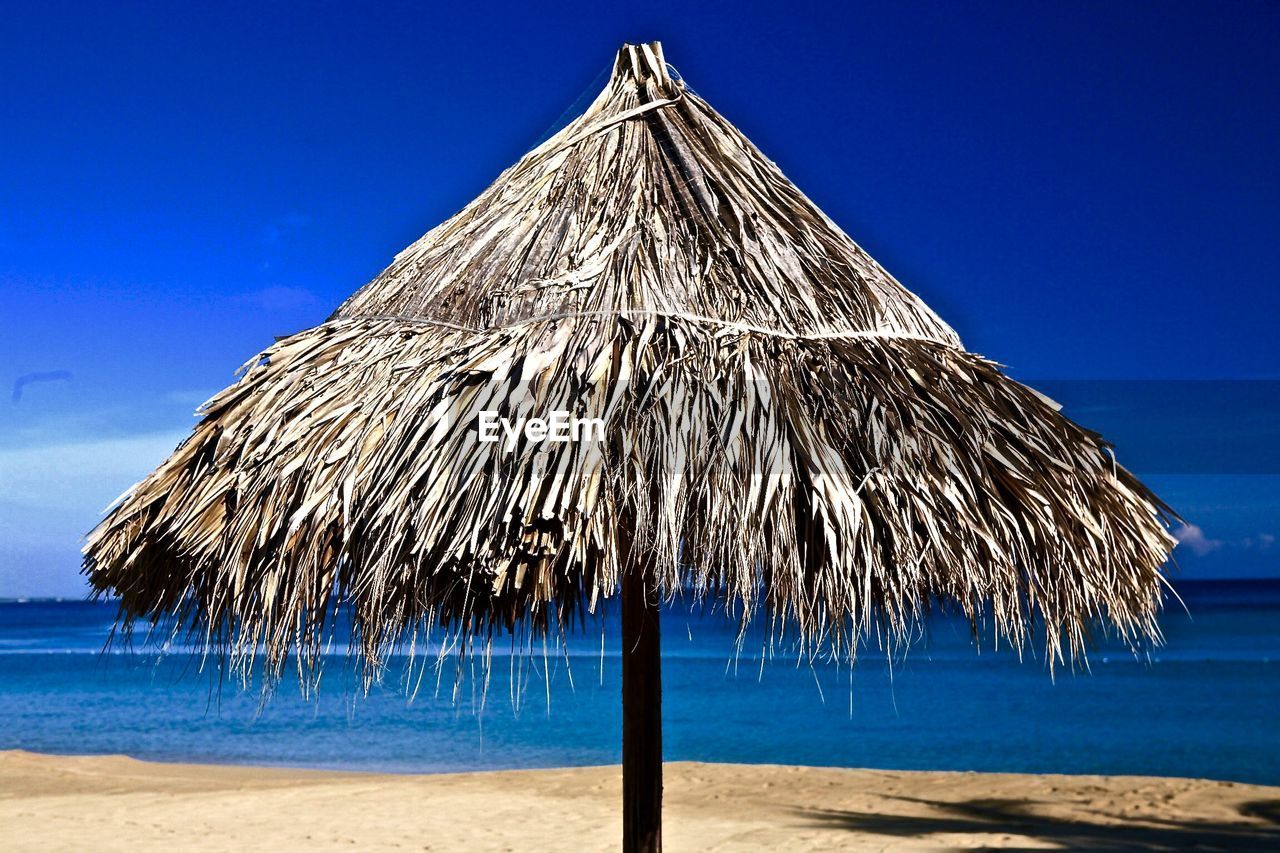 Thatched roof parasol on shore against blue sky