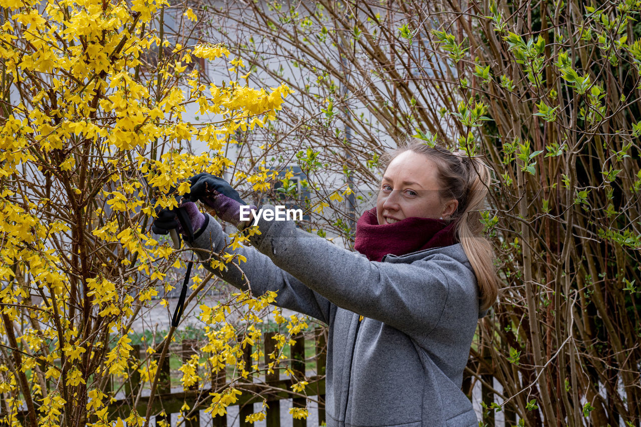 Side view of young woman trimming bushes in the spring garden.