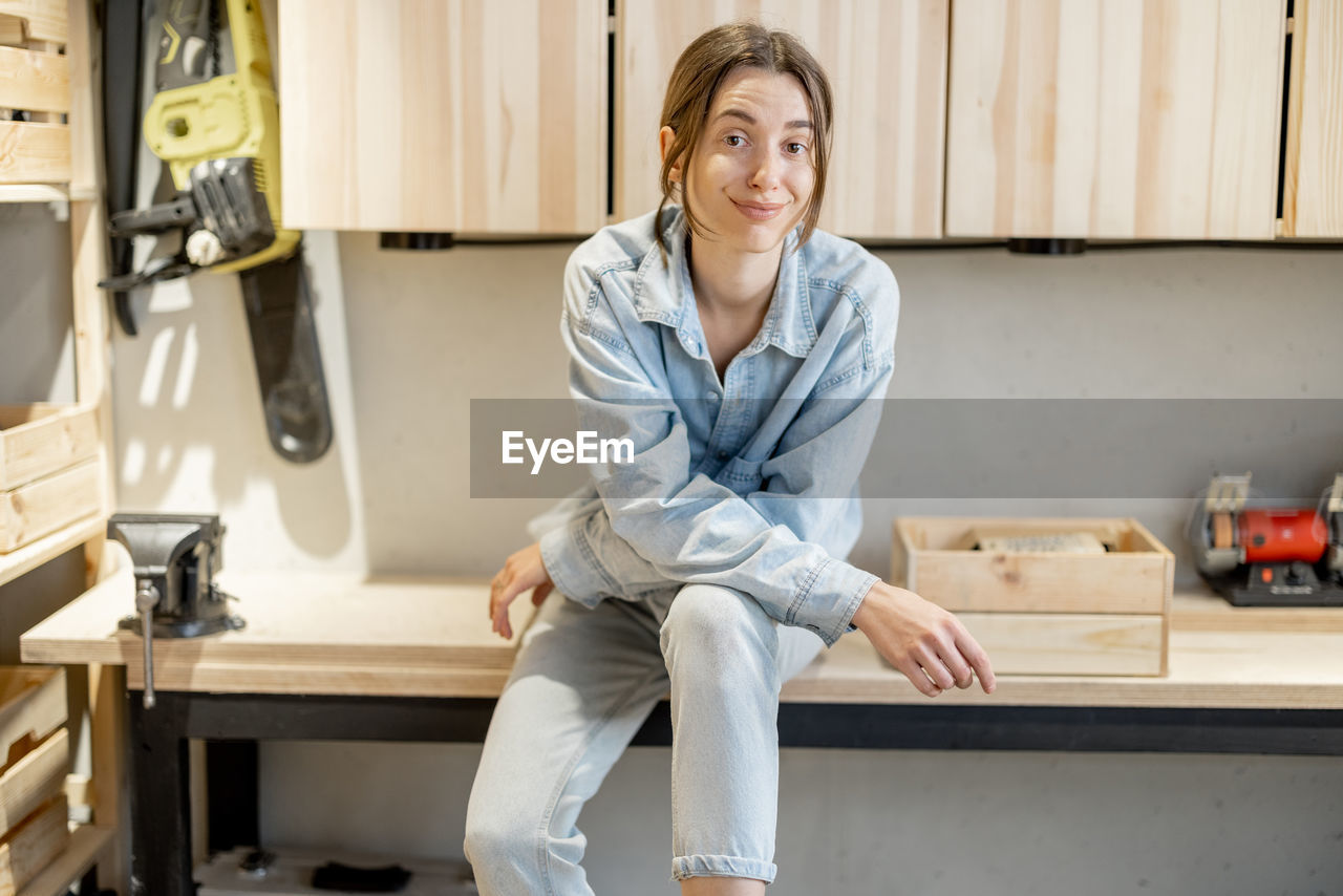 PORTRAIT OF SMILING WOMAN SITTING AT HOME