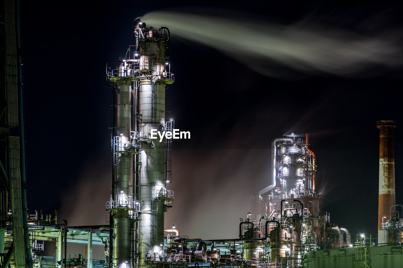 Illuminated industrial buildings against sky at night