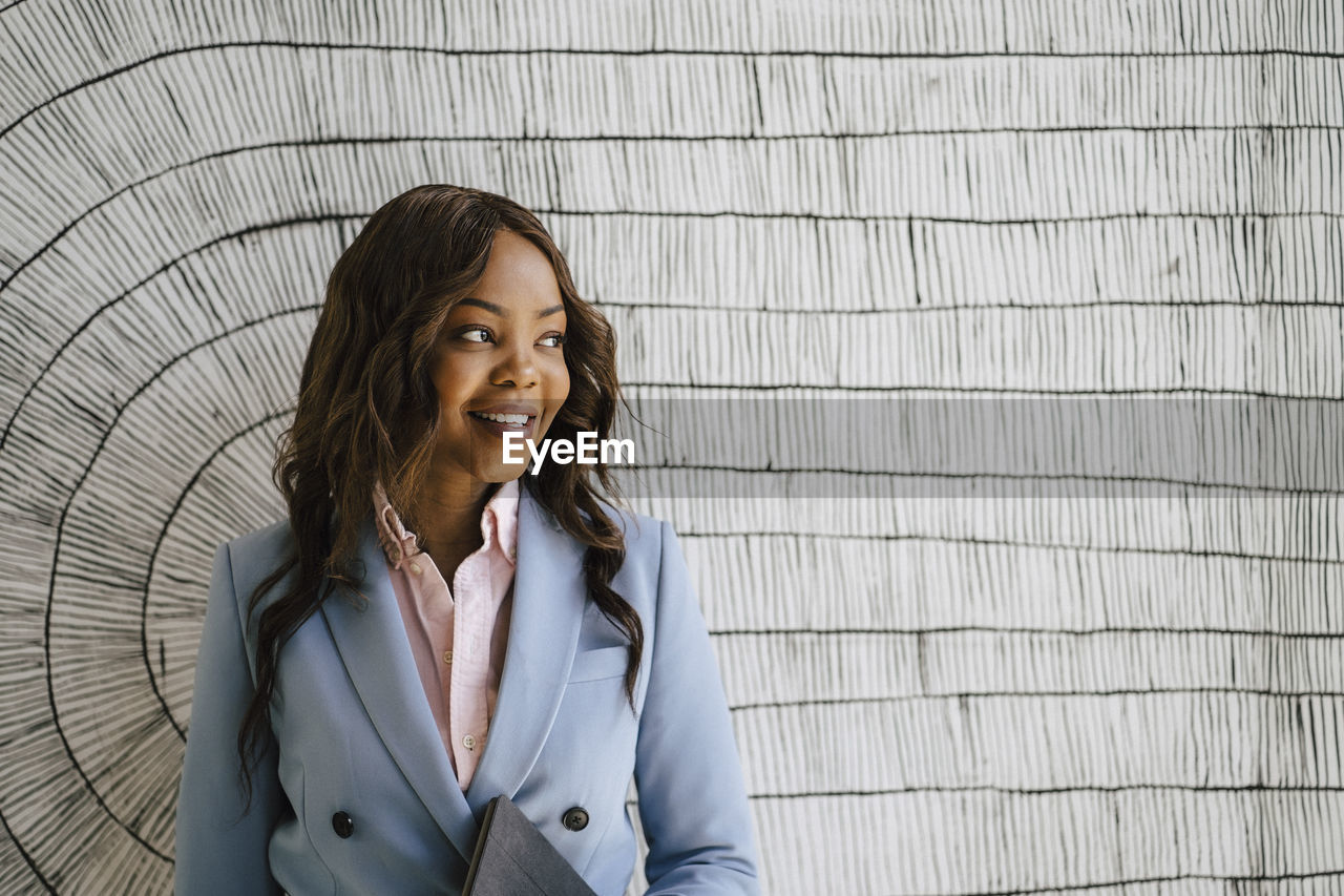 Smiling businesswoman looking away while standing against wall