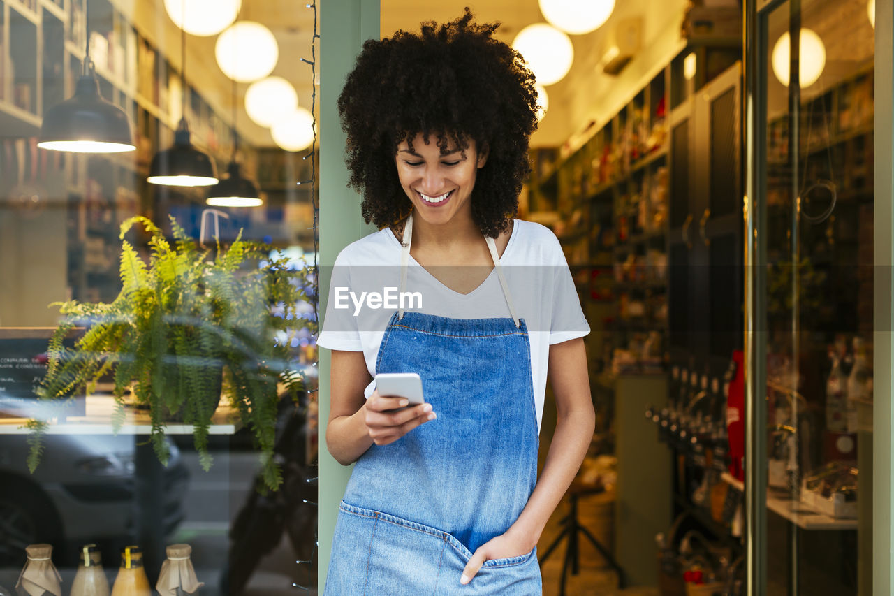 Smiling woman using cell phone in entrance door of a store