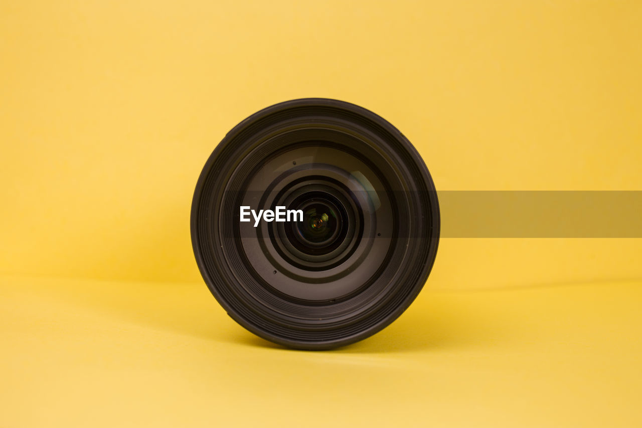 Close-up of camera lens against yellow background