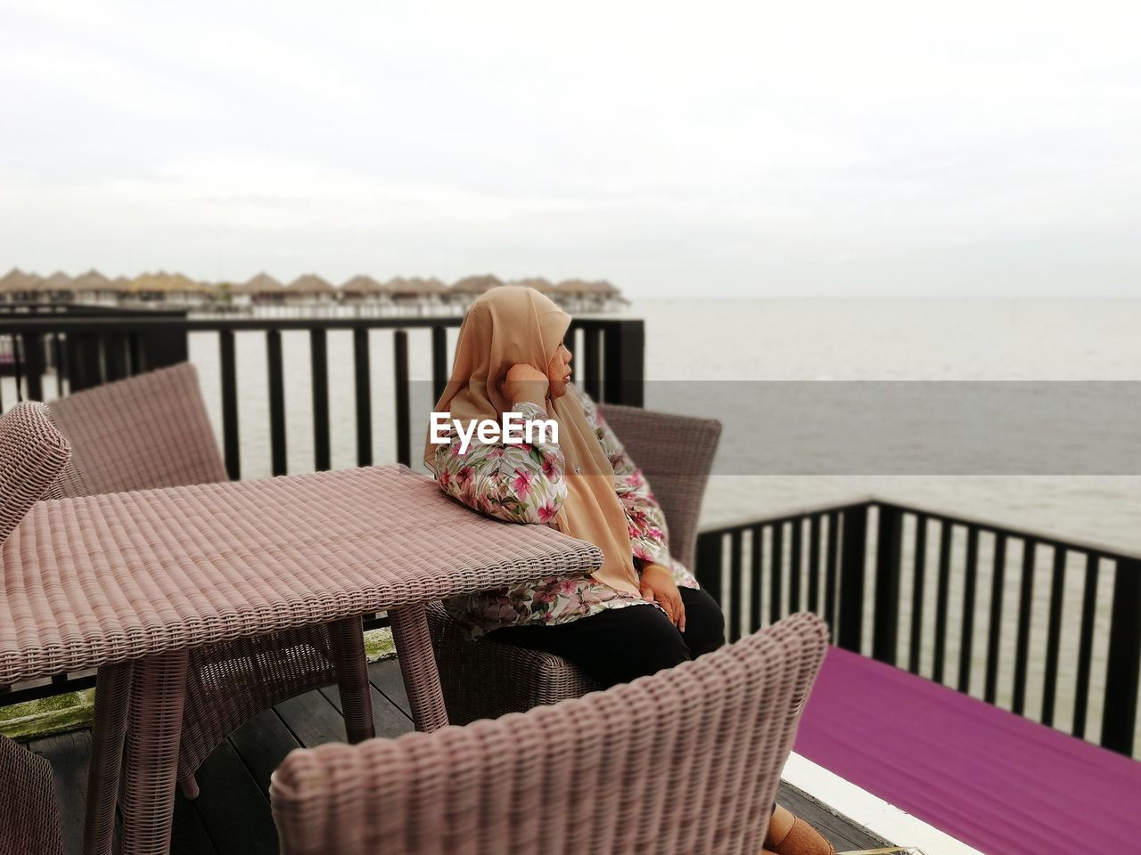 Woman sitting at outdoor cafe by sea against sky