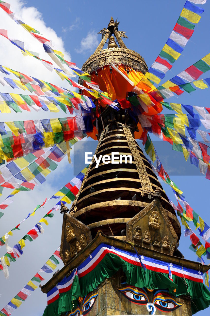 Low angle view of colorful buntings on spire at pashupatinath temple against sky