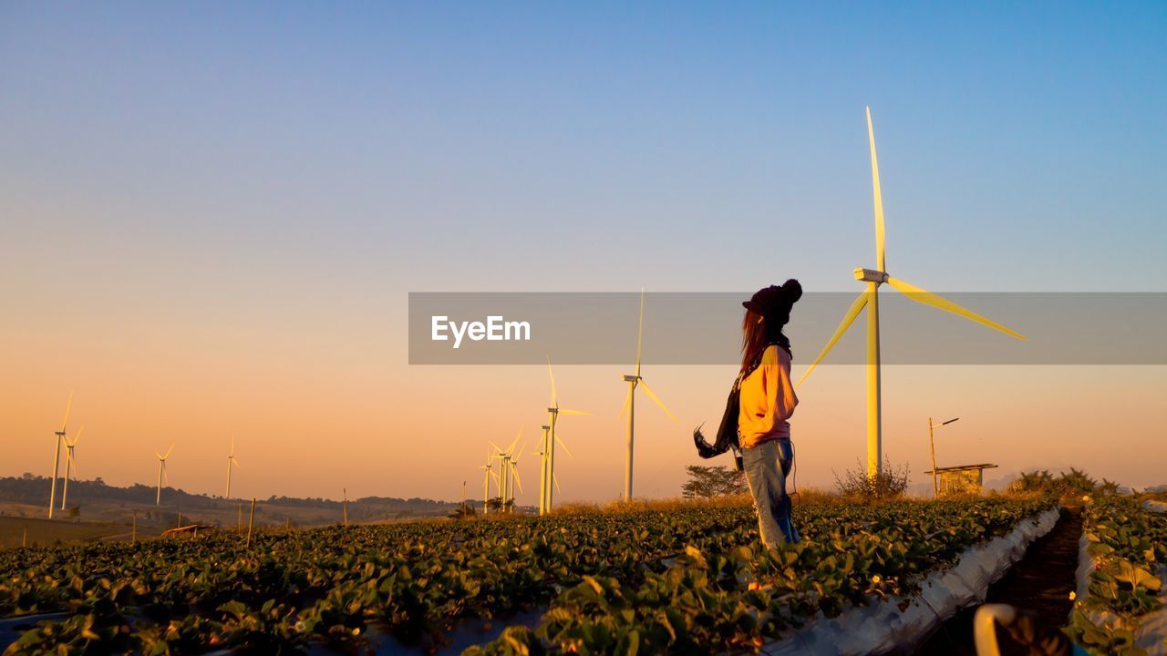 Side view of woman standing on field against clear sky during sunset