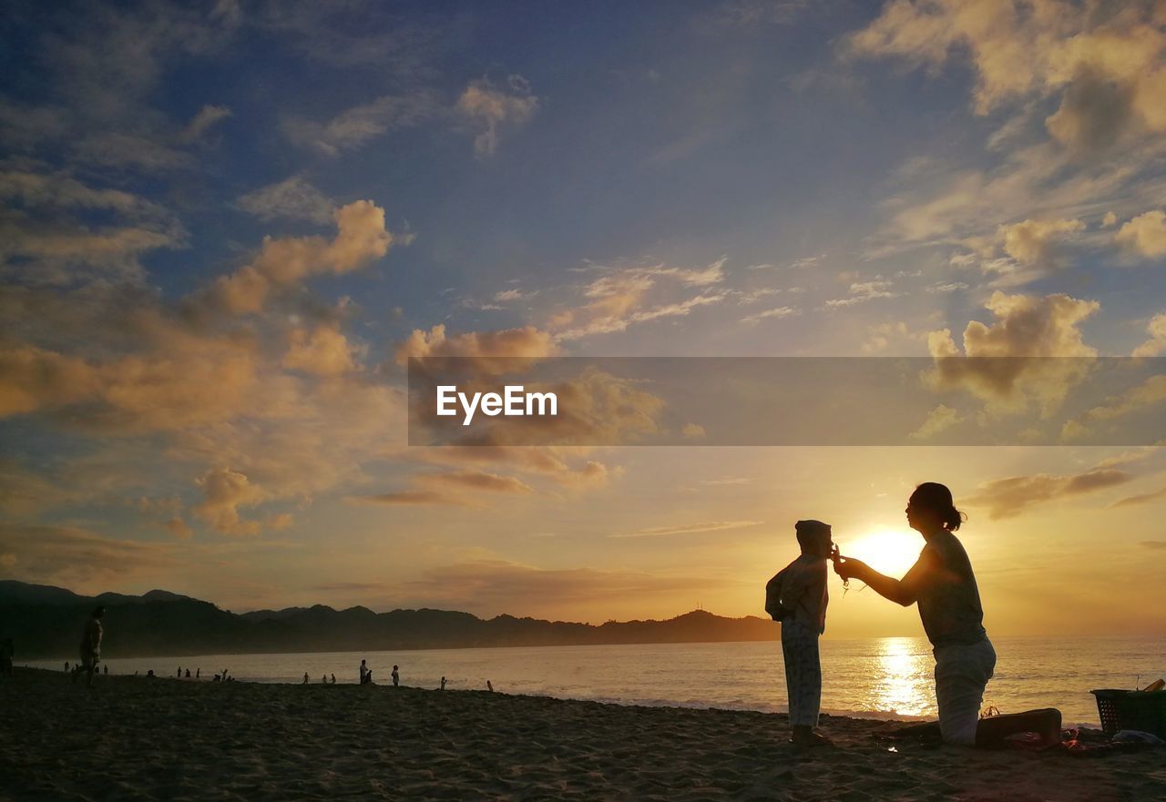 SILHOUETTE MEN STANDING ON BEACH AGAINST SKY DURING SUNSET