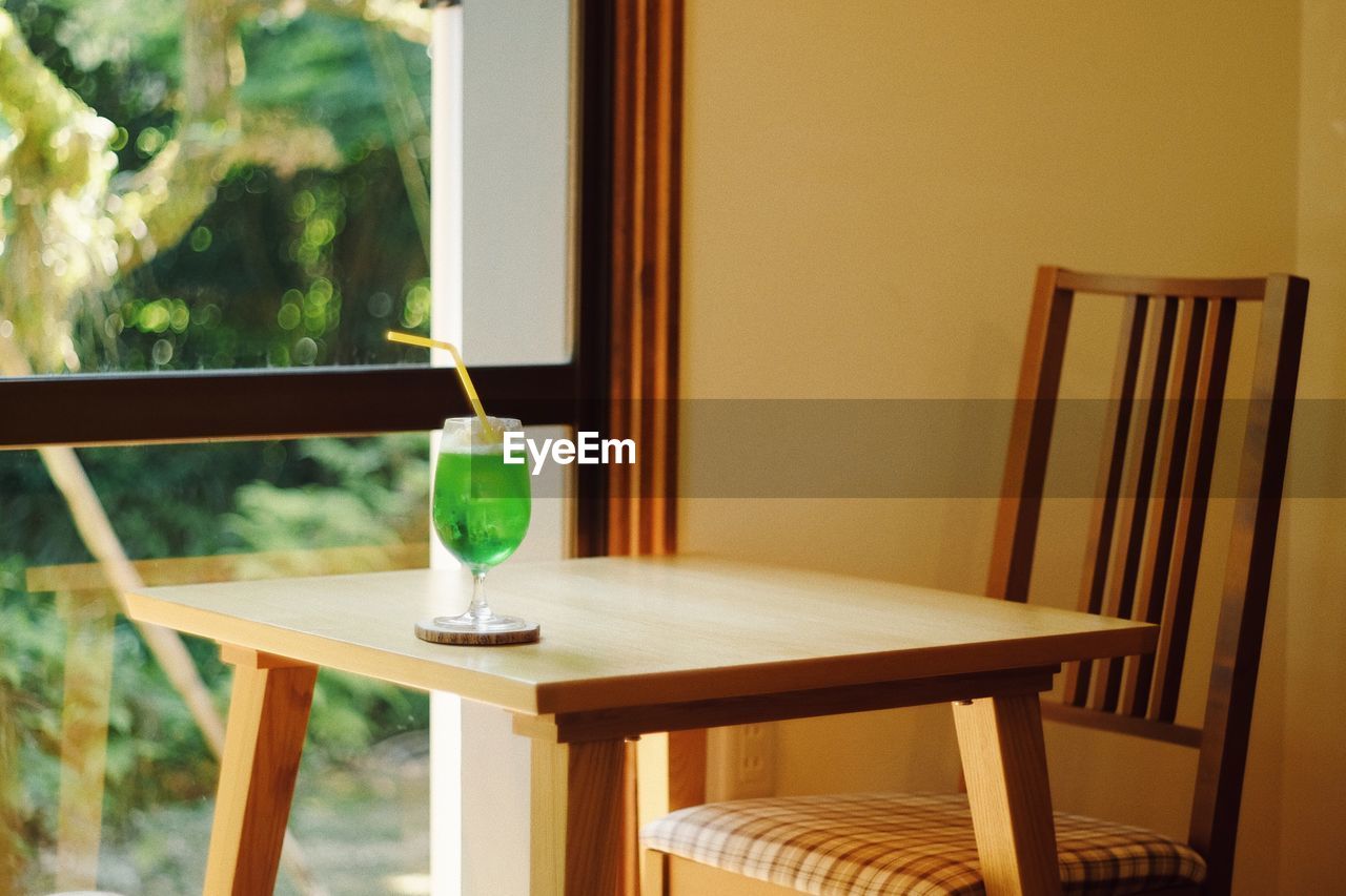 Drink with empty chair and table against window at home