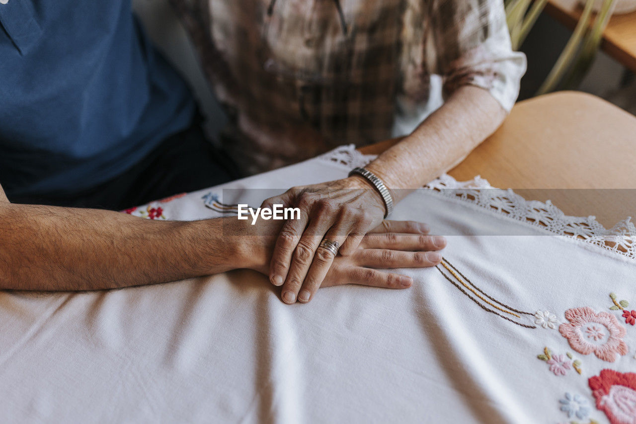 Senior woman holding hand of male caregiver over tablecloth at home