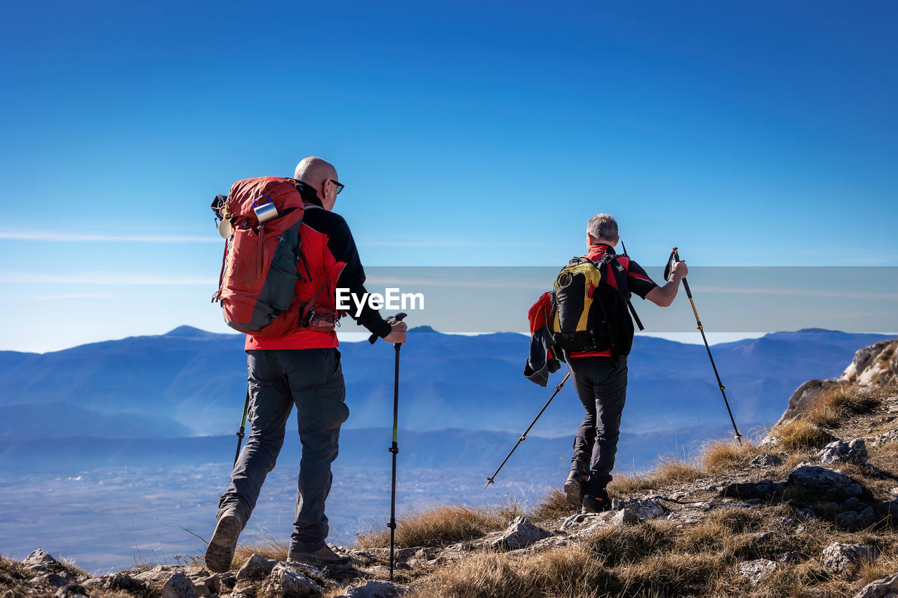 Rear view of two men standing on mountain against clear blue sky