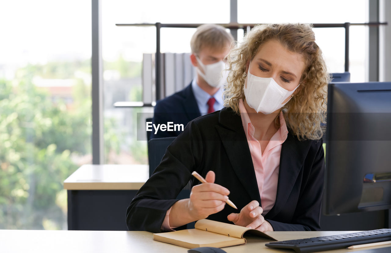 Businesswoman wearing mask writing in diary