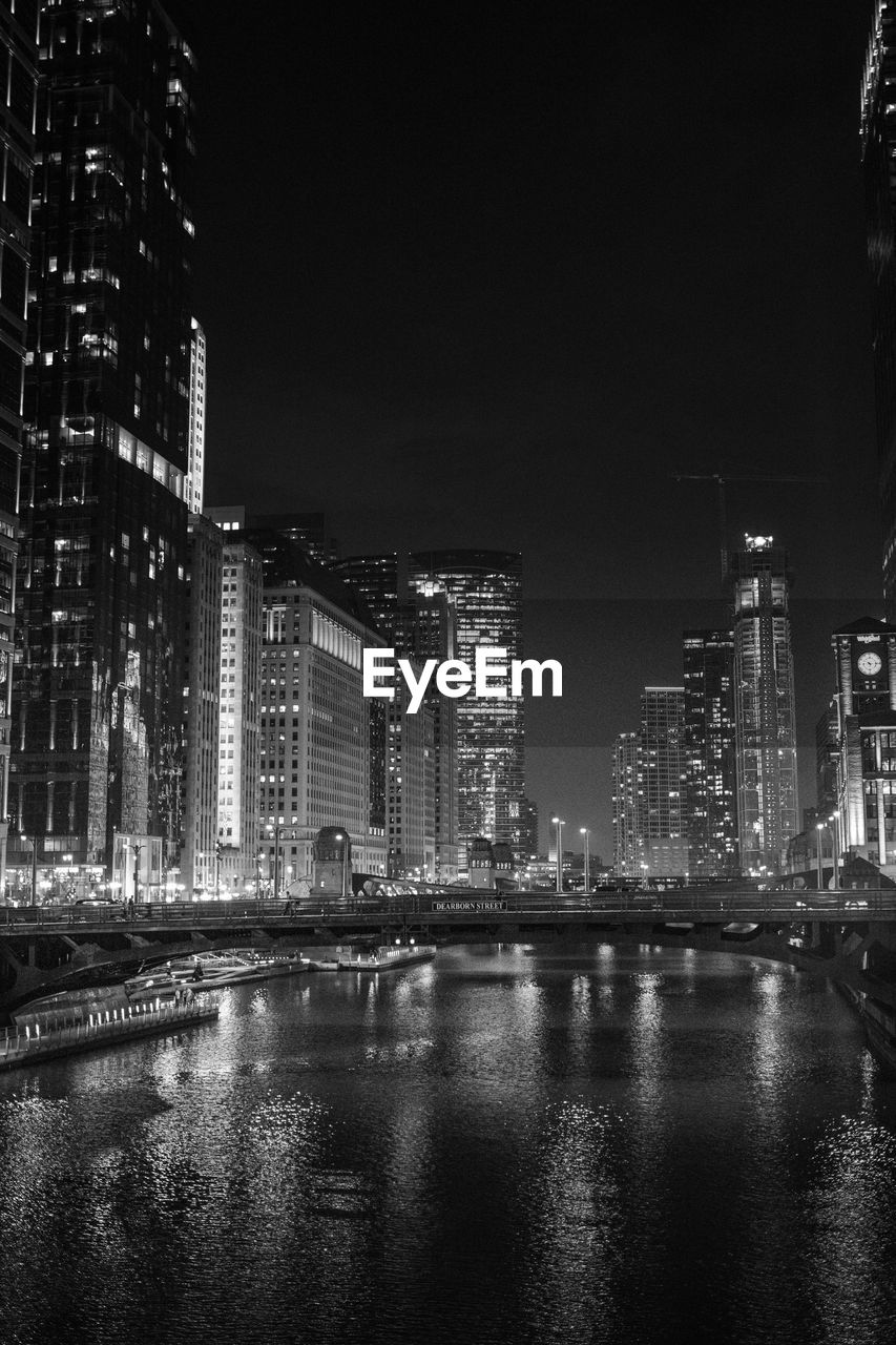 Illuminated buildings by river against sky at night