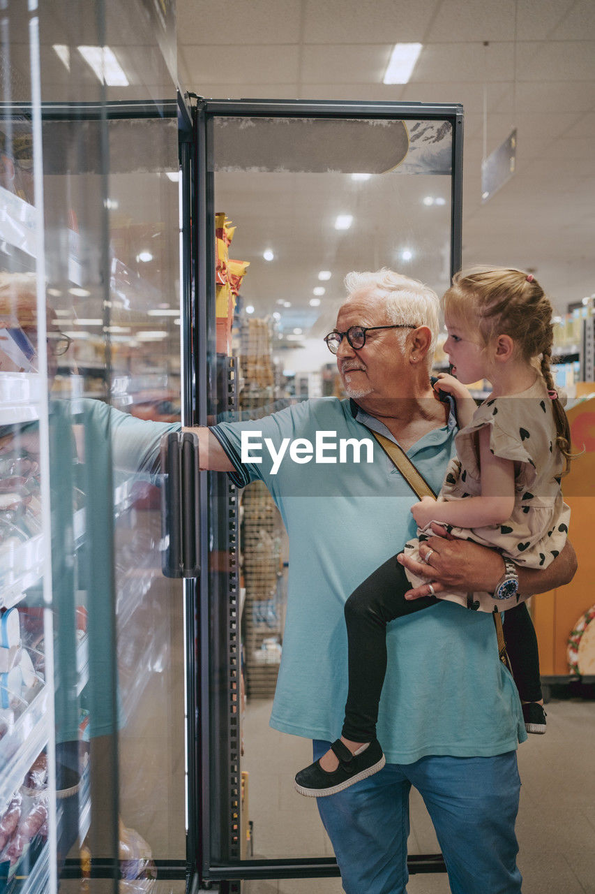 Senior man carrying granddaughter while doing shopping at grocery store