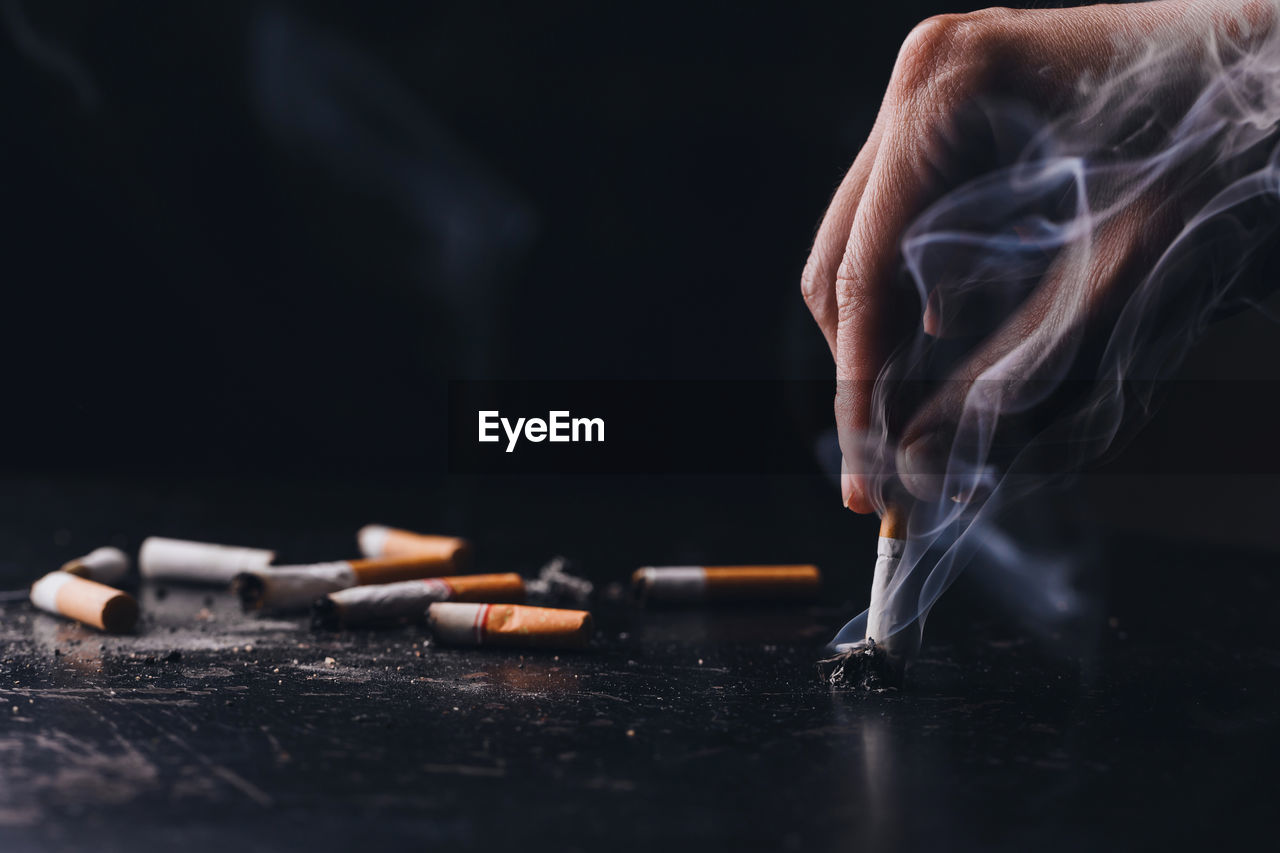 Cropped hand of person holding cigarette against black background