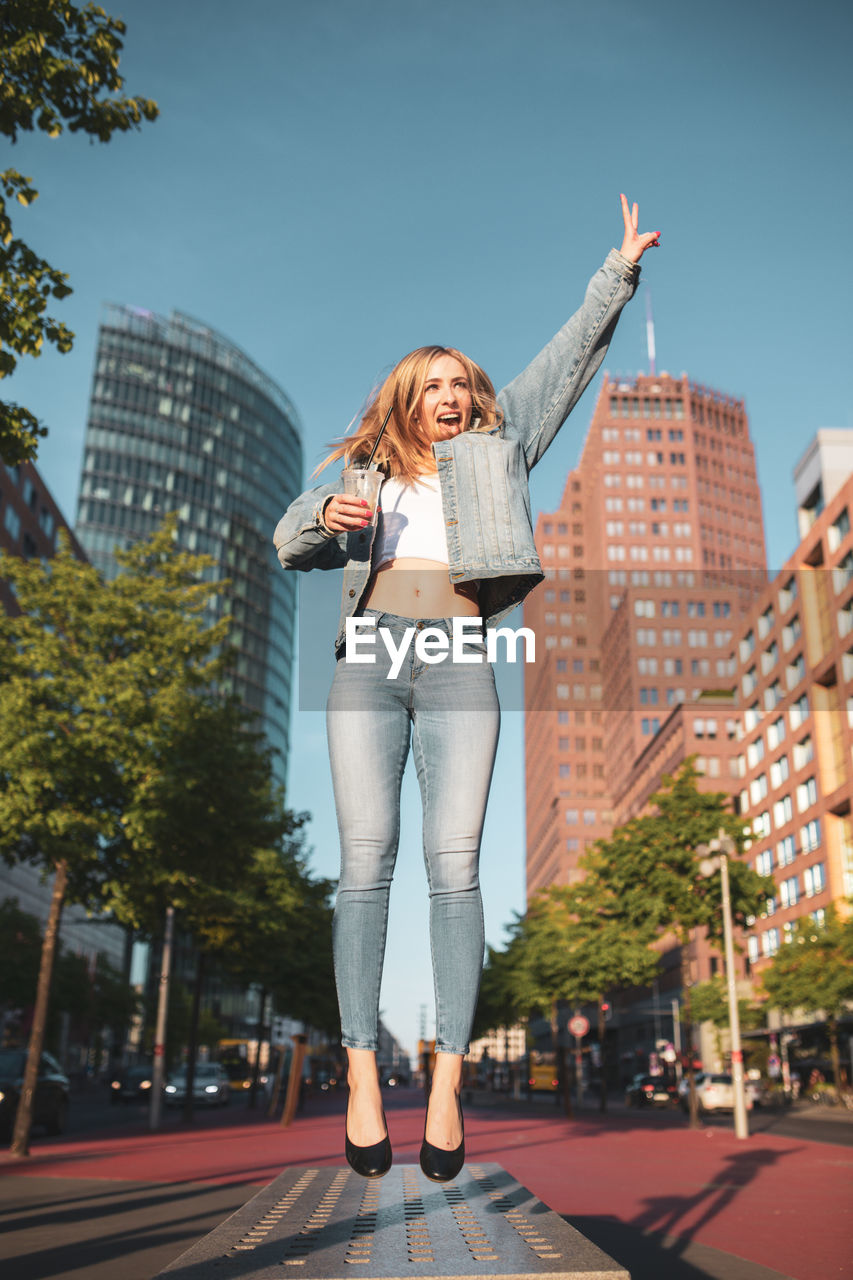 Full length of woman jumping against buildings in city