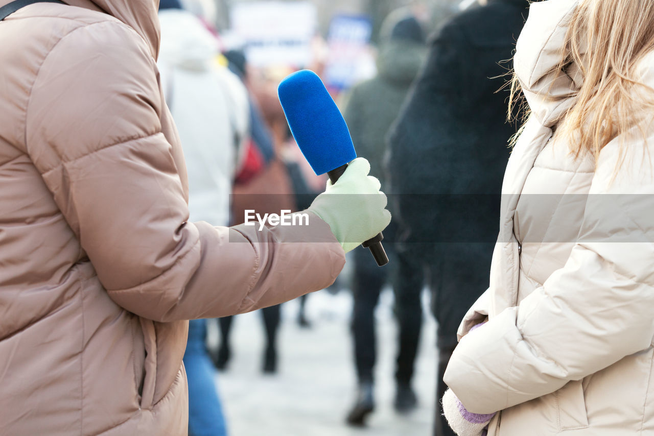 Media interview at street, journalist holding microphone interviewing unrecognizable person