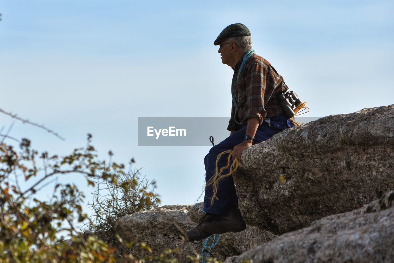 Mature man sitting of rock against sky