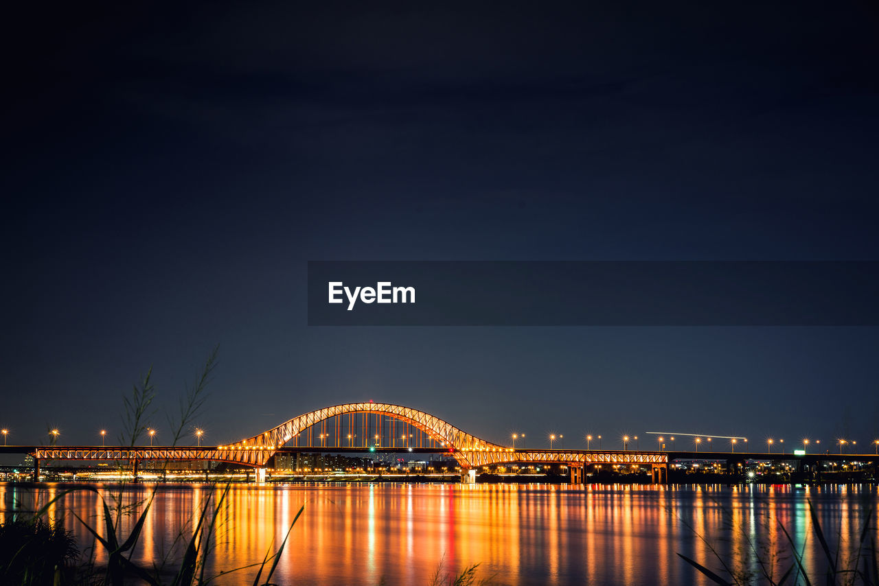 Illuminated bridge over river at night