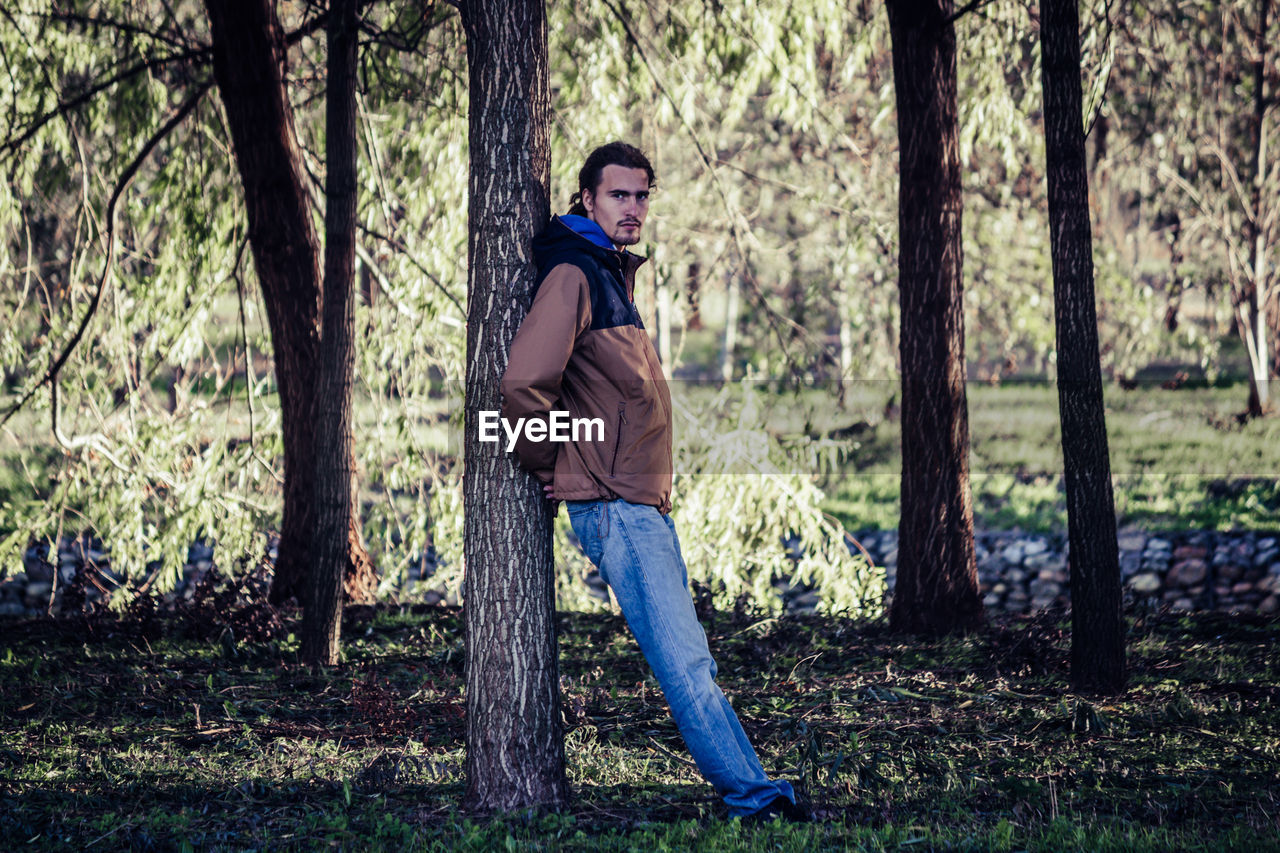 Portrait of man standing by tree trunk in forest