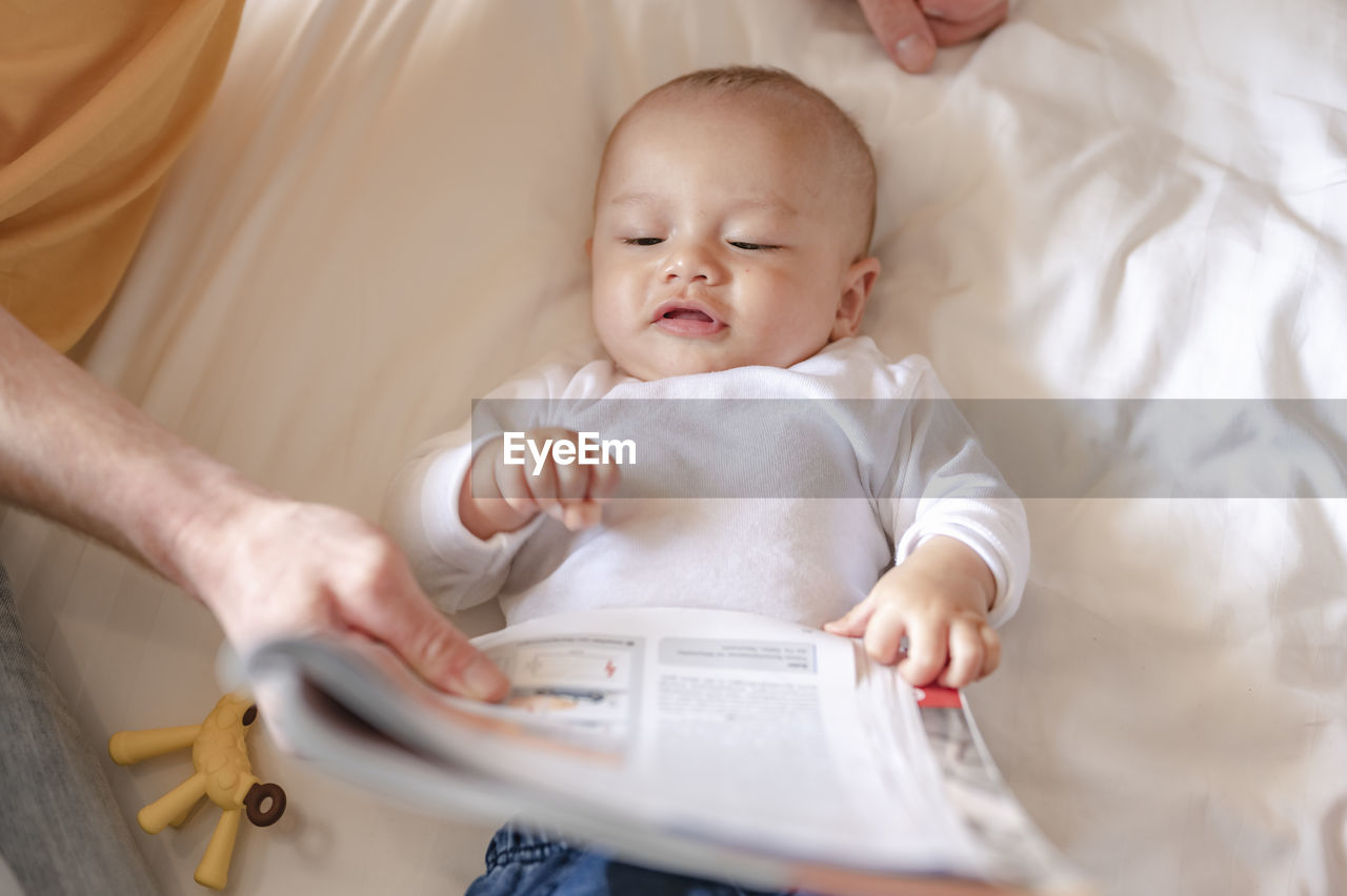 Father showing newspaper to baby on bed at home