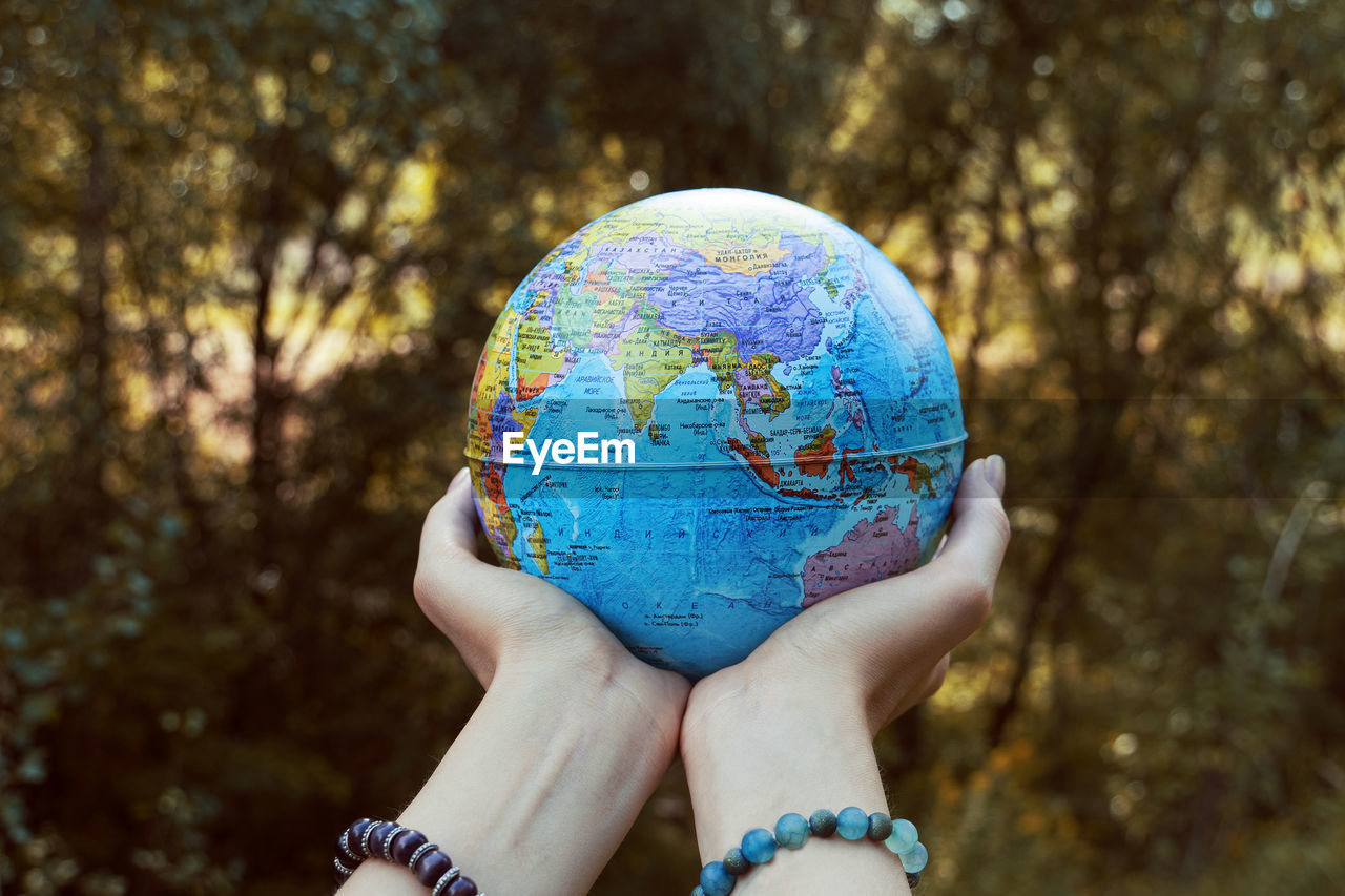 Woman holding globe against trees