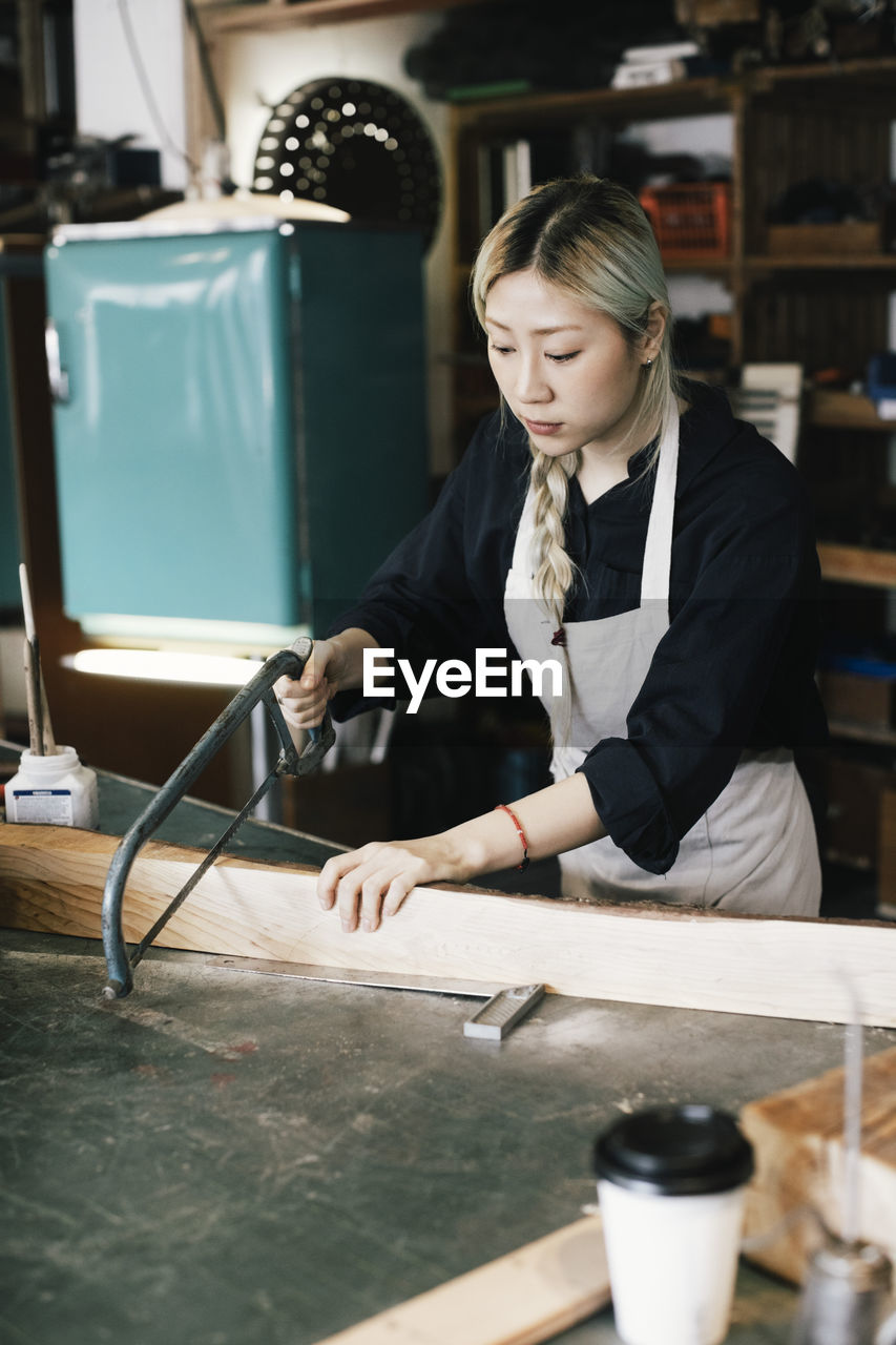 Young female entrepreneur cutting wood at workbench