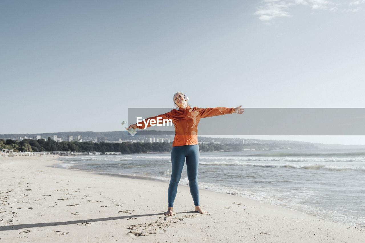 Mature woman standing with arms outstretched on beach