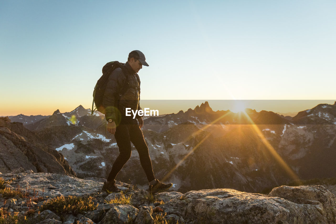 Adventurous man hiking along mountain ridge during sunset.