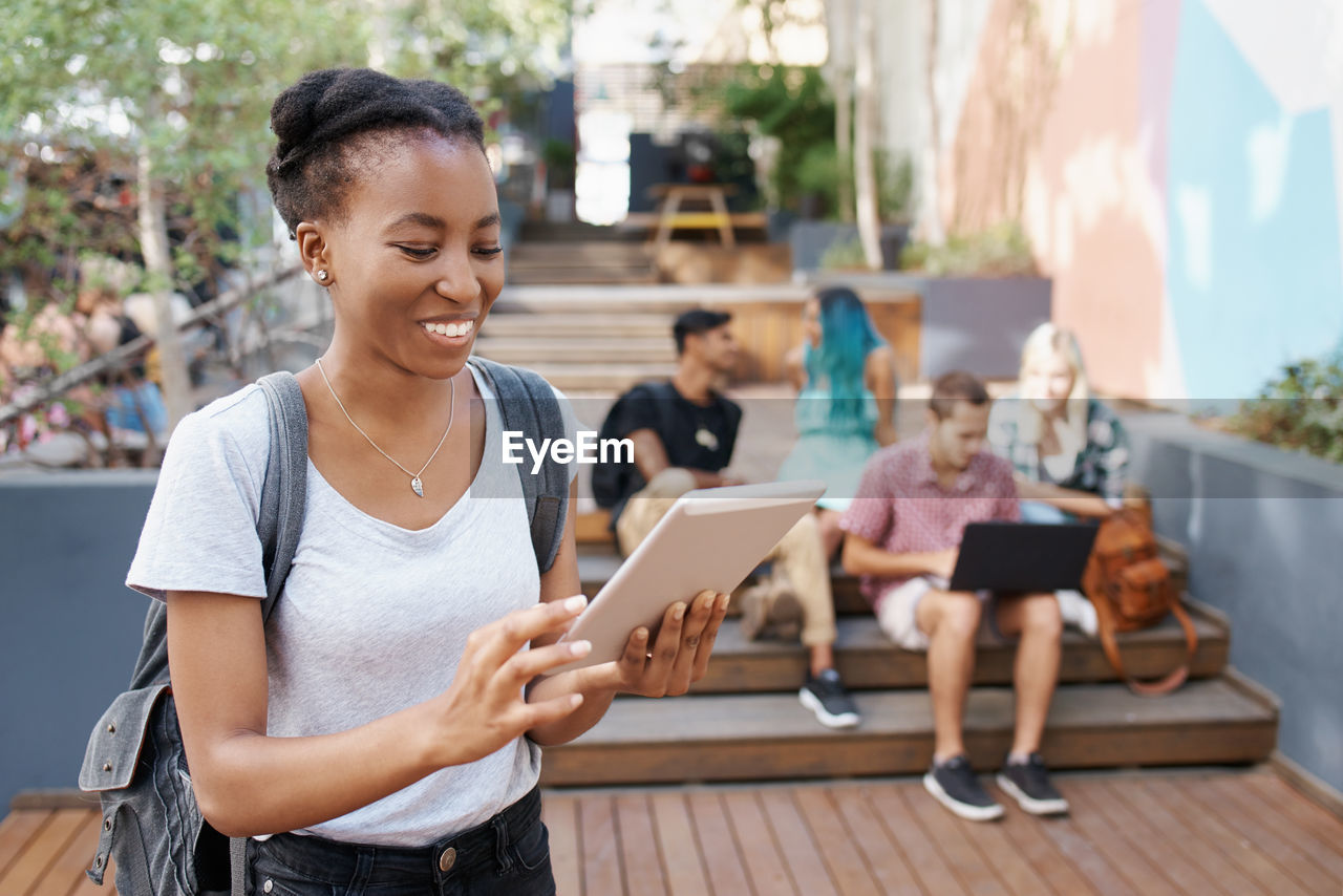 Young woman using digital tablet with friends in background