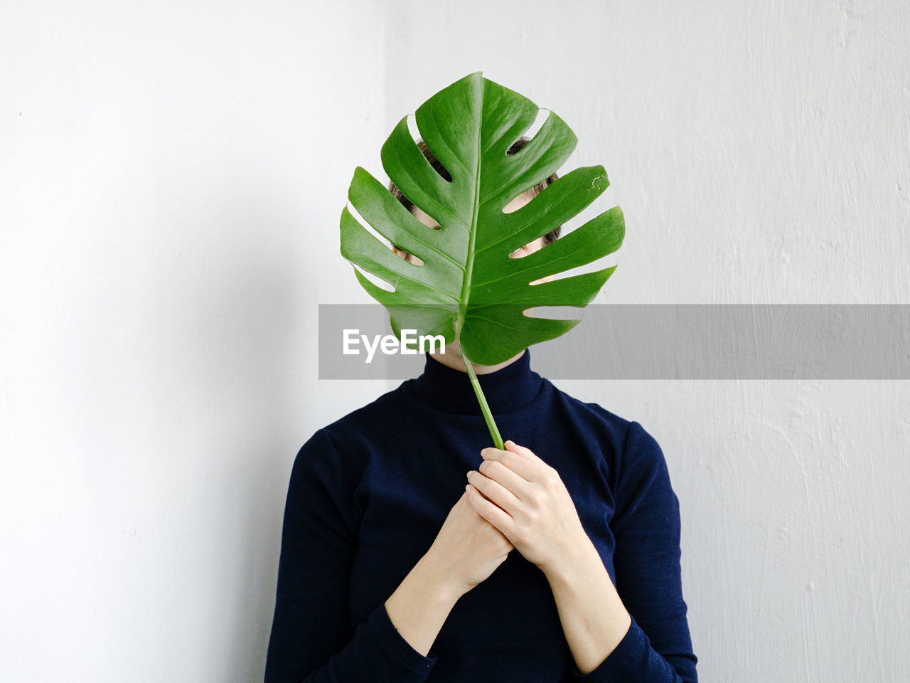 Woman covering face with leaf while standing against wall