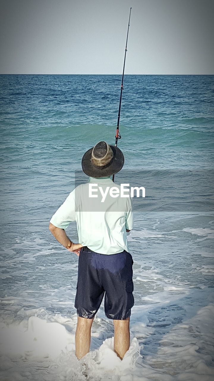 REAR VIEW OF MAN STANDING ON BEACH