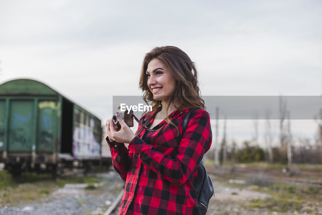 Smiling young woman photographing through camera at shunting yard