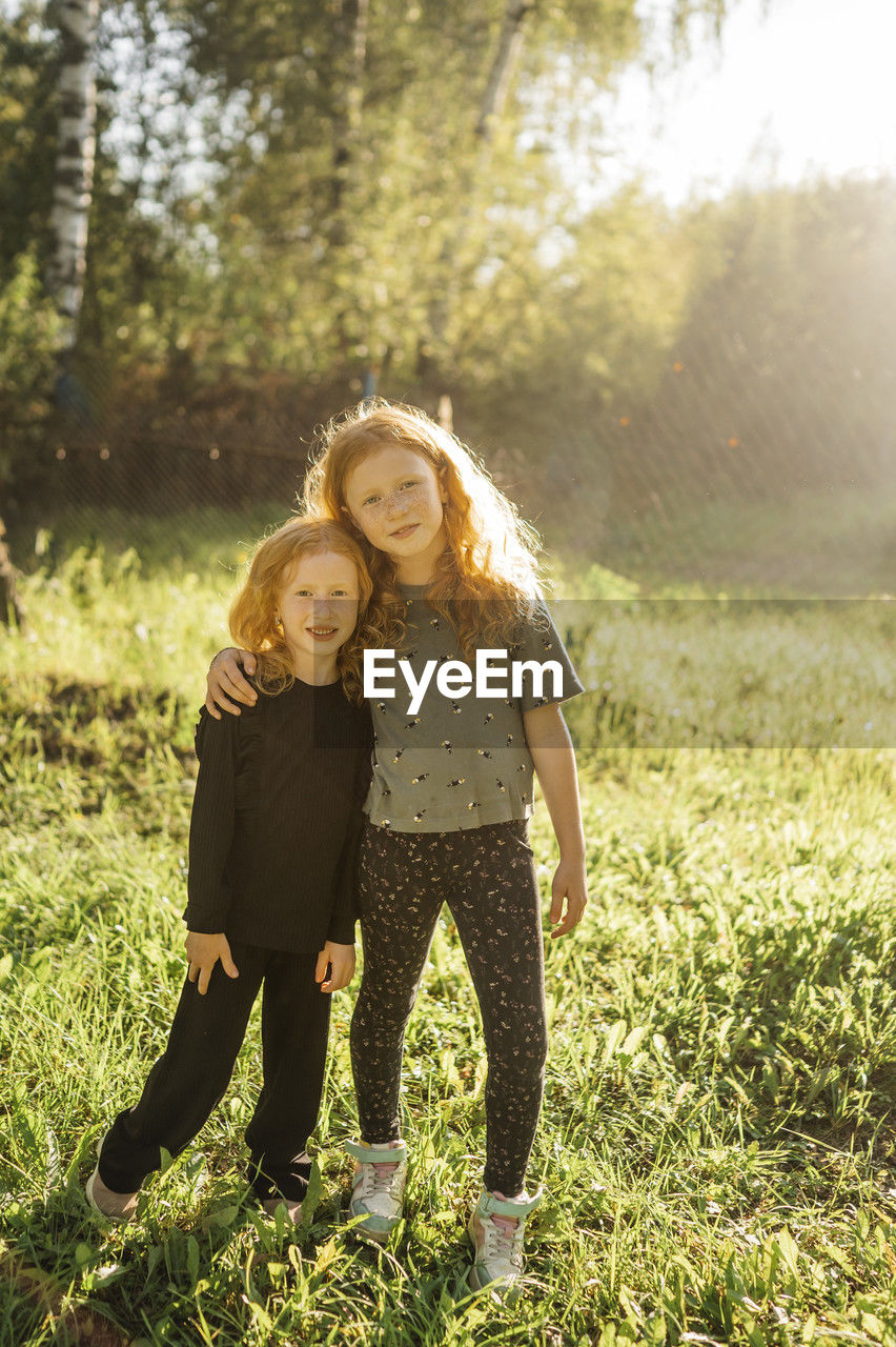 Smiling sisters standing in park on sunny day