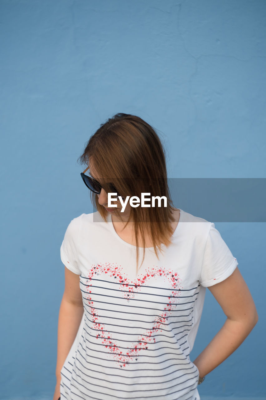 Beautiful woman wearing sunglasses while standing against blue wall