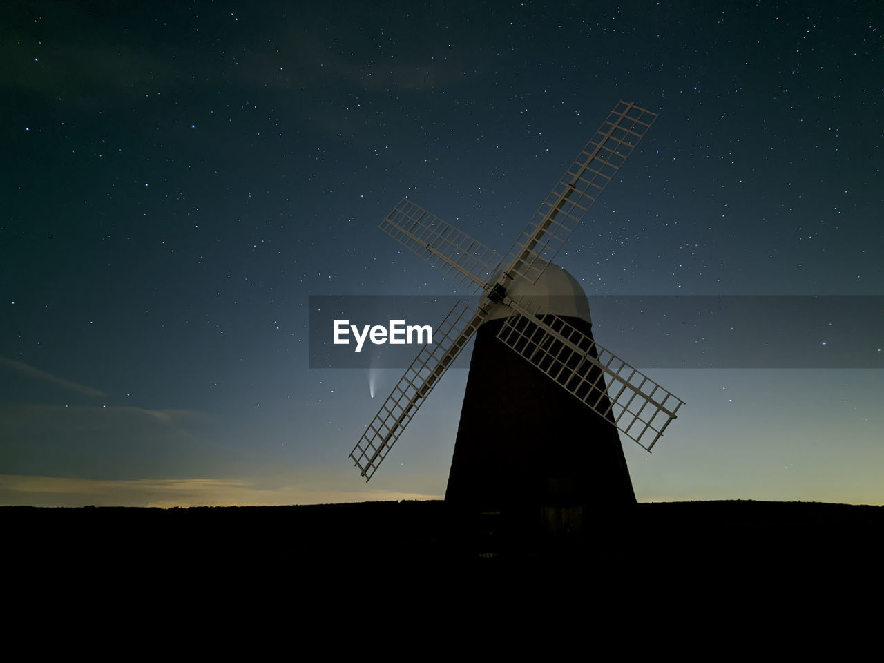 Traditional windmill on field against sky at night with comet neowise