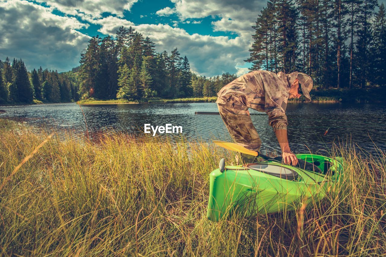 VIEW OF BOY STANDING ON GRASS BY LAKE