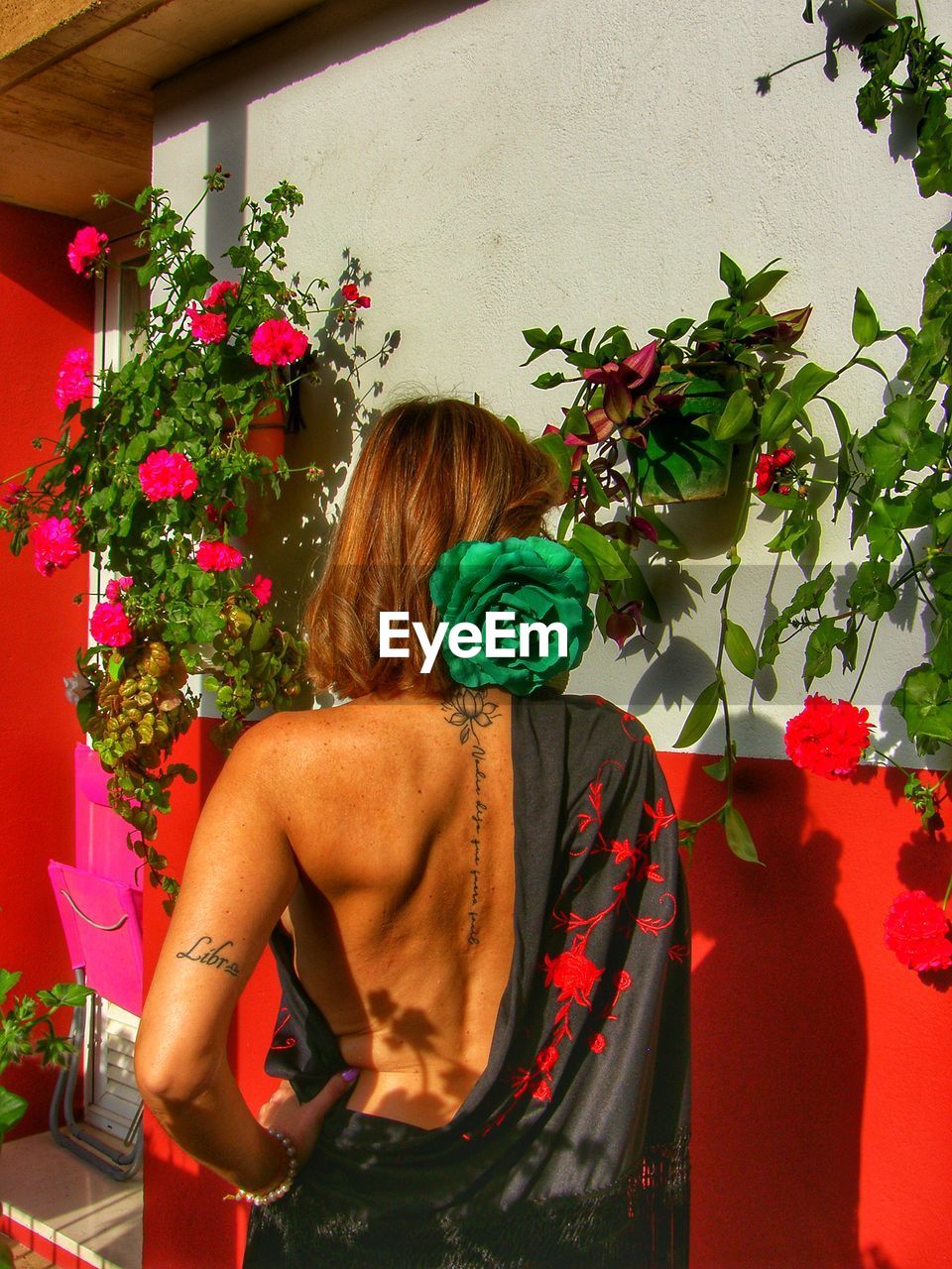 REAR VIEW OF WOMAN STANDING BY FLOWERING PLANTS