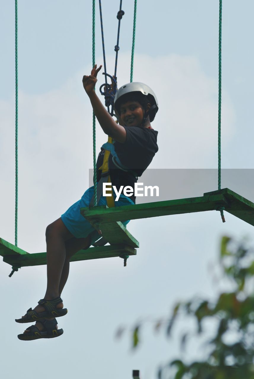 Low angle view of boy on rope course against sky