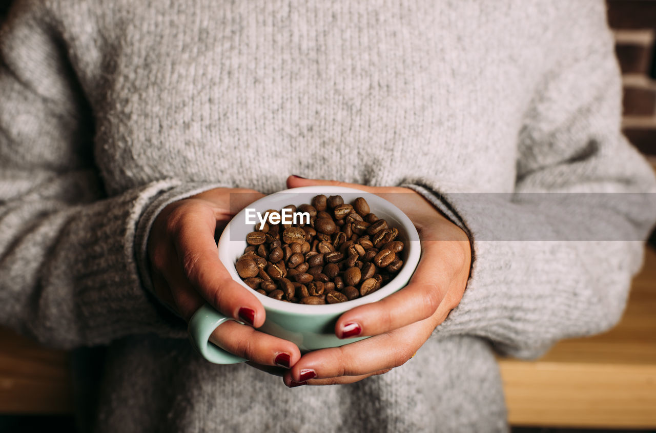 Woman with sweater holding coffee cup with coffee beans inside