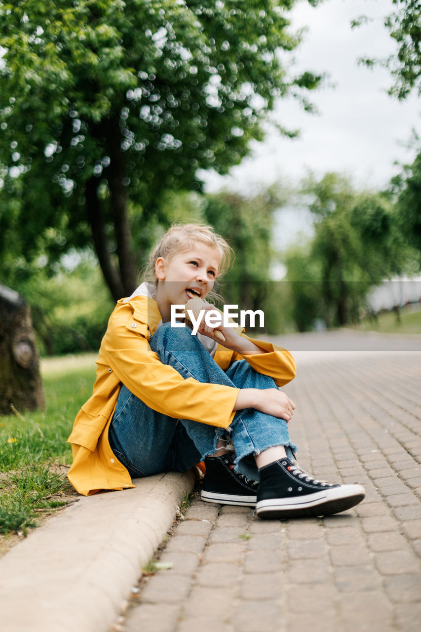 Boy looking away while sitting on plant against trees