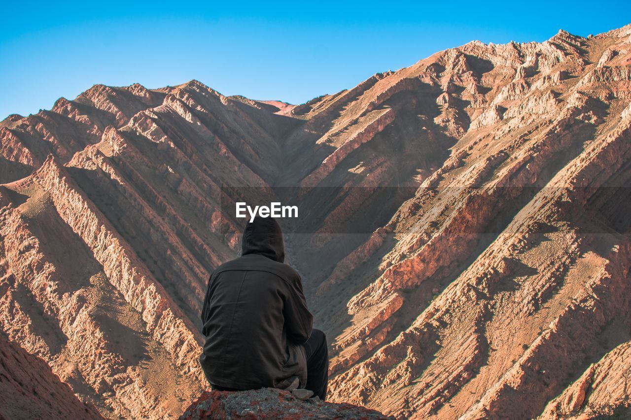 Rear view of man sitting against rocky mountains