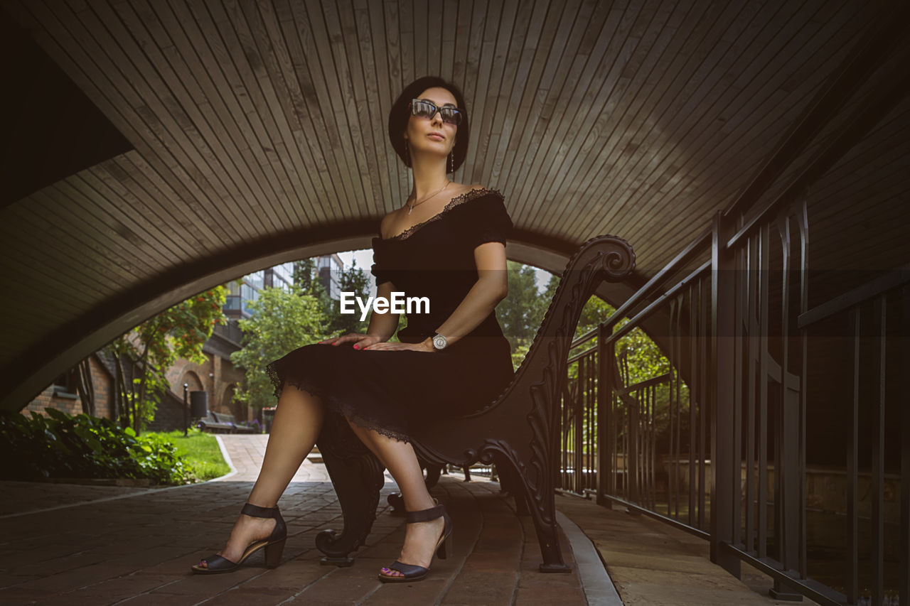 A pretty charming middle-aged woman in a black dress and sunglasses strolls through the city park