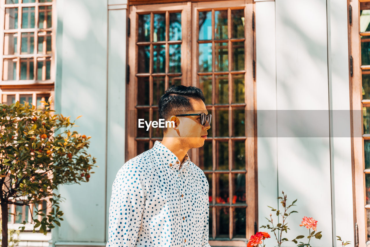 Young man wearing sunglasses while standing against window