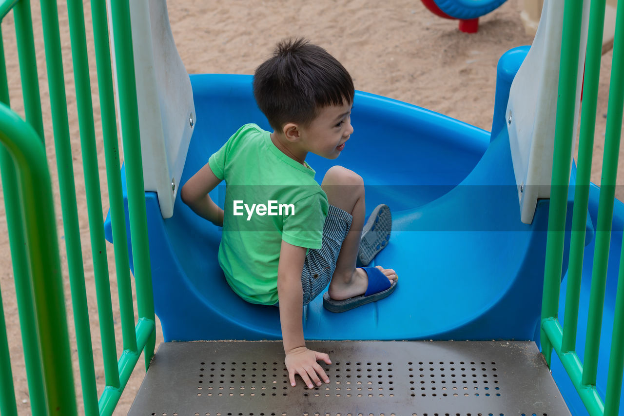 High angle view of boy sitting on slide in playground