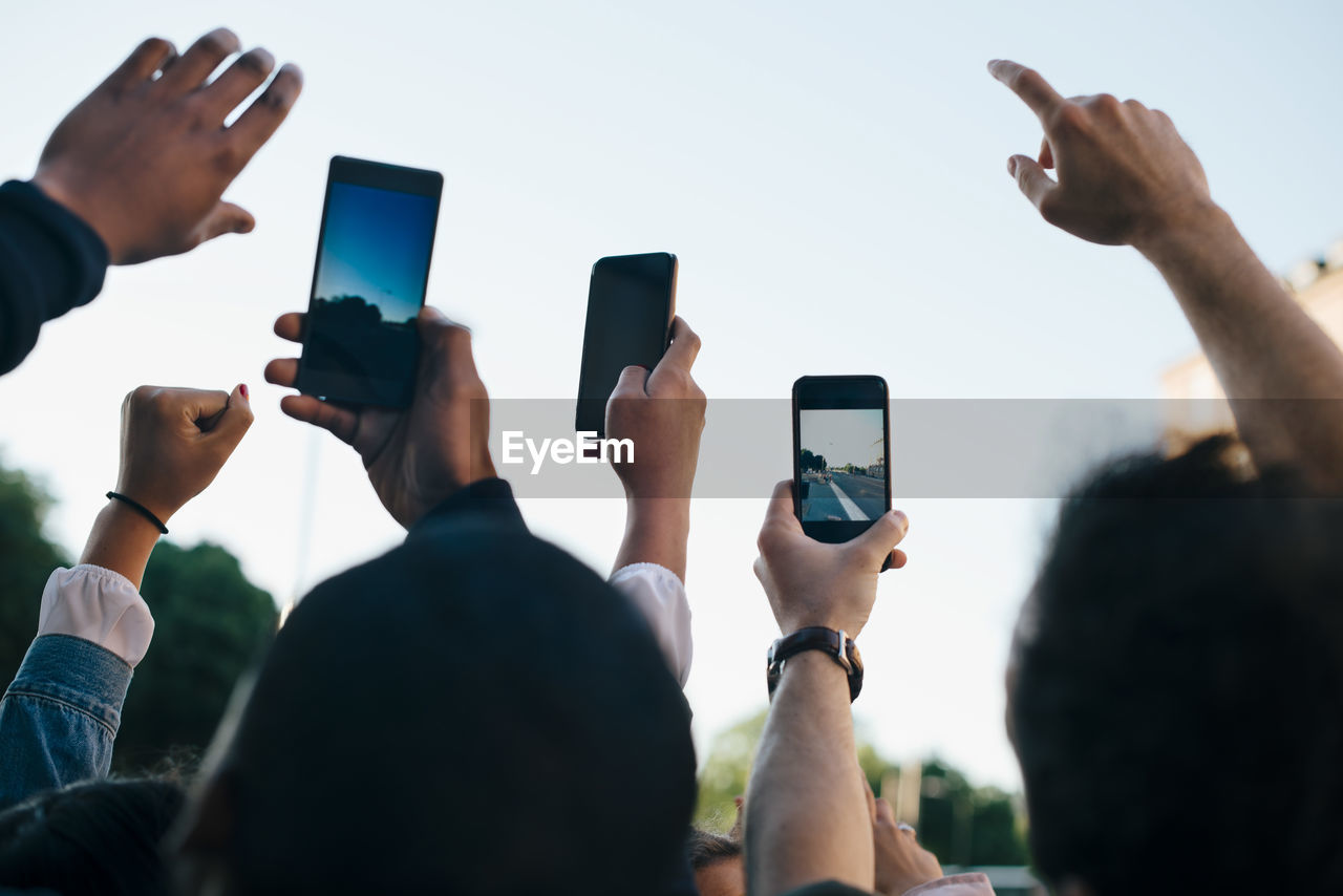 Low angle view of friends photographing from smart phones against sky