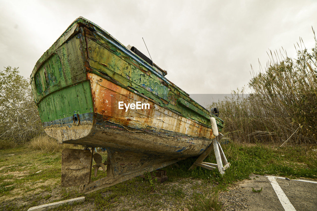 transportation, sky, vehicle, abandoned, nature, cloud, nautical vessel, mode of transportation, boat, rural area, damaged, plant, rundown, water, old, no people, grass, land, overcast, wood, transport, outdoors, day, decline, deterioration, environment, landscape, architecture, watercraft, waterway, weathered, broken, rural scene, bad condition, ruined, beach