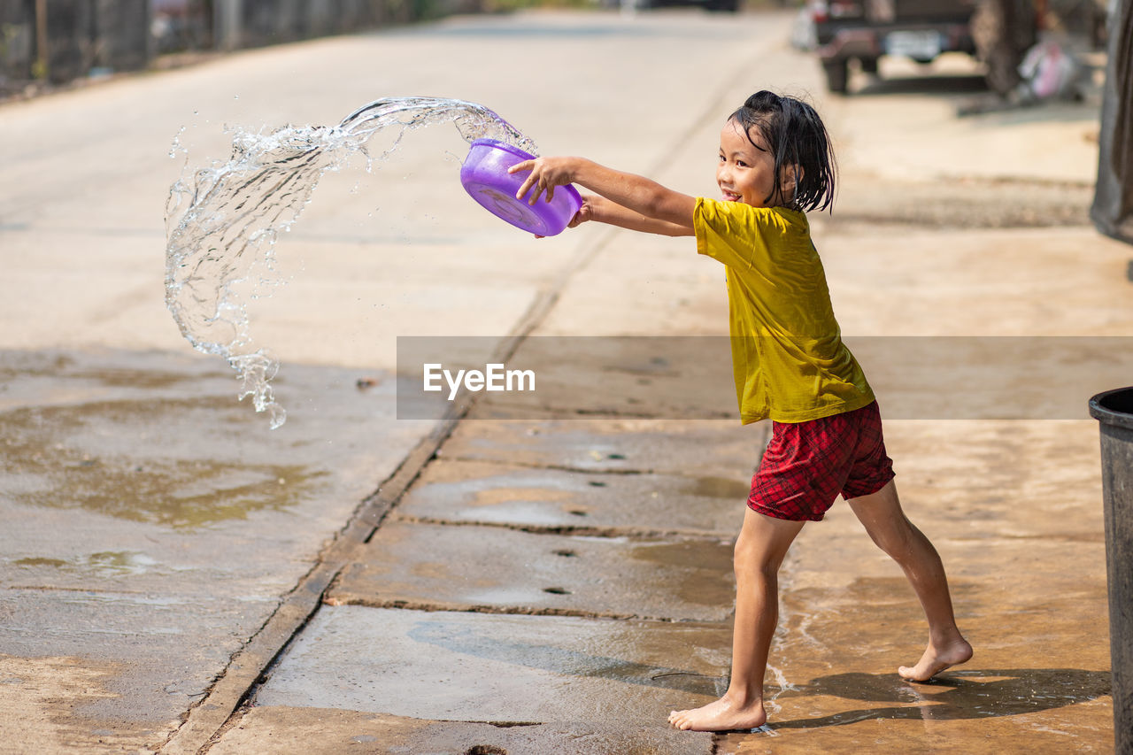 Side view of girl pouring water on road