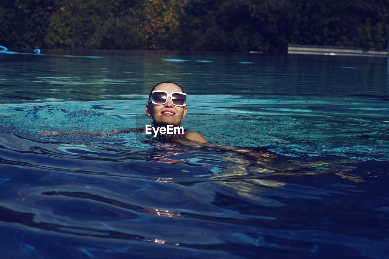 A vintage photo of a woman in a black swimsuit and white sunglasses swimming in the pool