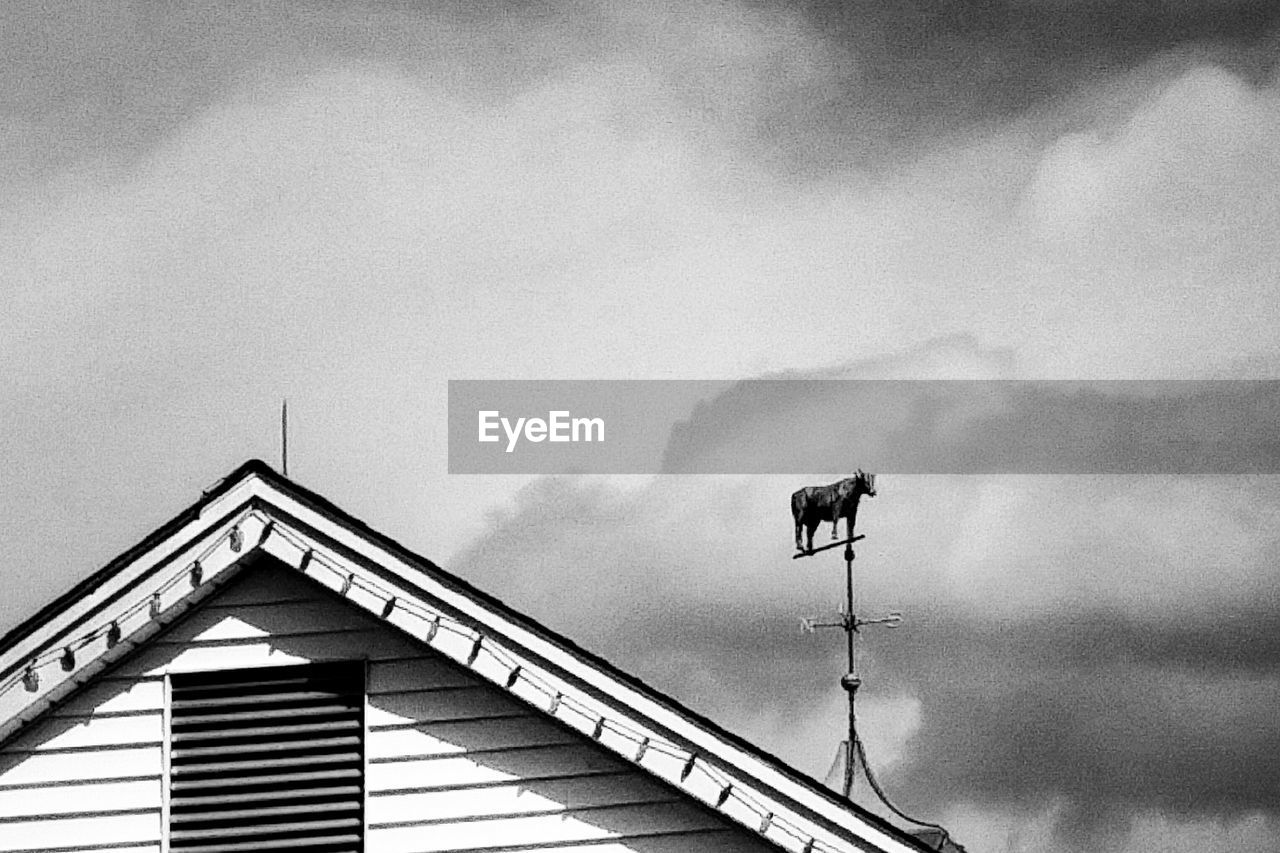 Low angle view of cow statue on weather vane against cloudy sky