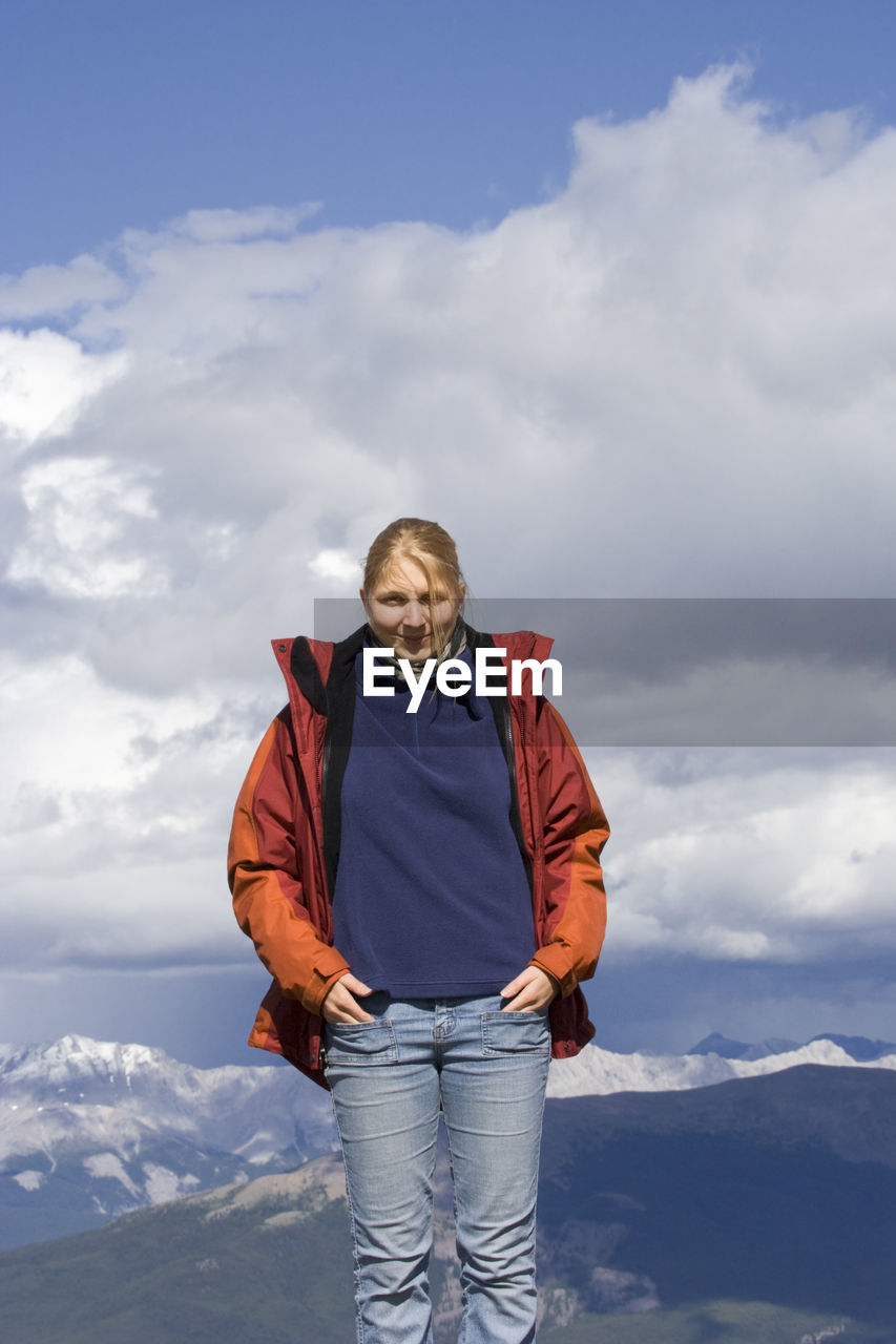 Portrait of woman standing on whistler mountain against cloudy sky during winter